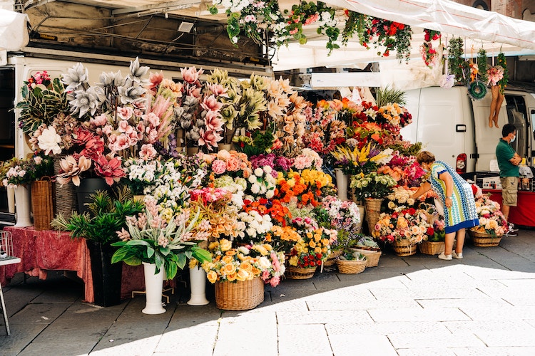 A flower stall at an outdoor market in Tuscany, Italy, overflowing with vibrant blooms.